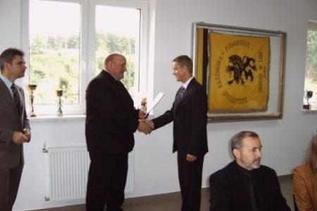Dwaj mężczyźni w garniturach ściskają dłonie podczas wręczenia stypendiów.