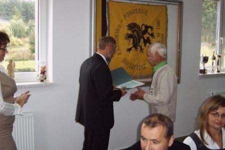 Wręczenie stypendium studentowi przez urzędnika, w tle flaga, inni obserwują.