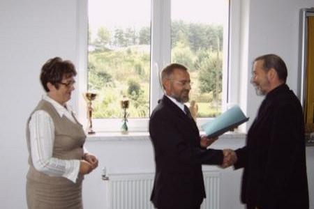 Wręczenie stypendium studentowi przez urzędnika, kobieta stoi z boku.