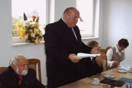 Mężczyzna w garniturze wręcza dokumenty studentowi podczas ceremonii stypendialnej.