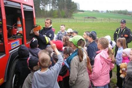 Strażak OSP Strzepcz pokazuje wóz strażacki grupie dzieci na pokazie.