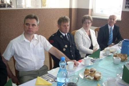 Uczestnicy Zjazdu OSP siedzą przy stole, jeden z nich w mundurze.