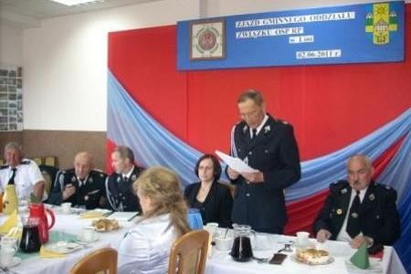 Zjazd OSP 2011: Mężczyzna w mundurze przemawia do zebranych przy stołach.