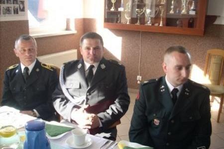 Delegaci OSP w mundurach siedzą przy stole na zjeździe.