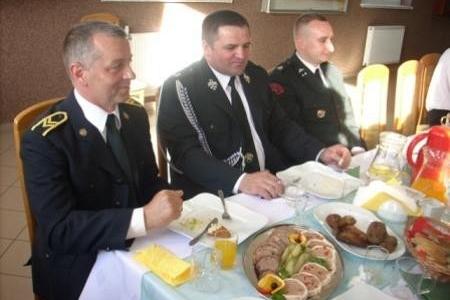 Delegaci OSP w mundurach siedzą przy zastawionym stole podczas zjazdu.