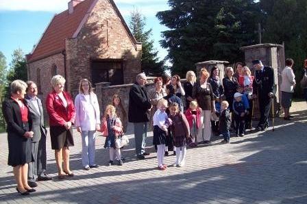 Mieszkańcy Lewina, dorośli i dzieci, stoją przed budynkiem, gotowi do uroczystości OSP.