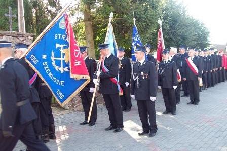 Strażacy OSP Lewino w szyku z niebieskim sztandarem na czele.