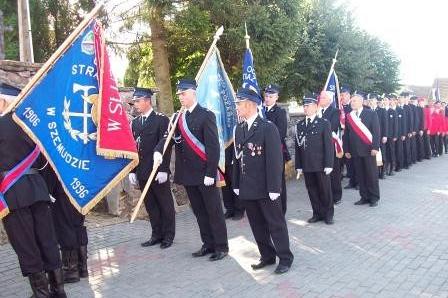 Strażacy z OSP Lewino w mundurach z pocztami sztandarowymi w uroczystej formacji.