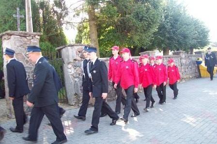 Młodzież z OSP Lewino w czerwonych strojach maszeruje w uroczystej paradzie.