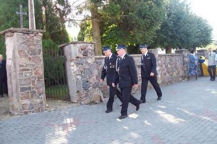 Strażacy OSP Lewino w mundurach idą obok muru.