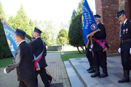 Strażacy OSP Lewino z dwoma sztandarami stoją i maszerują podczas uroczystości.