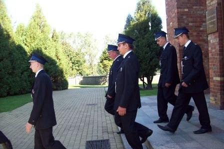 Członkowie OSP w galowych strojach idą na uroczystość wręczenia sztandaru.