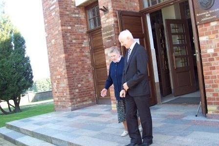 Dwóch mężczyzn przed kościołem po uroczystości, zapewne związanej ze sztandarem OSP Lewino.