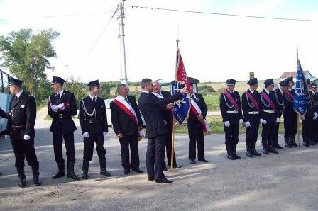 Grupa strażaków OSP Lewino w mundurach podczas ceremonii ze sztandarem.