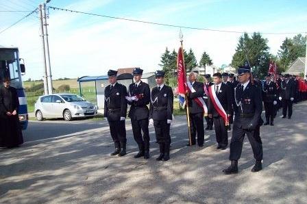 Strażacy OSP Lewino w mundurach na uroczystości pod sztandarem.