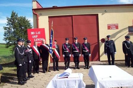 Strażacy OSP Lewino ze sztandarem przed remizą, podczas uroczystości.