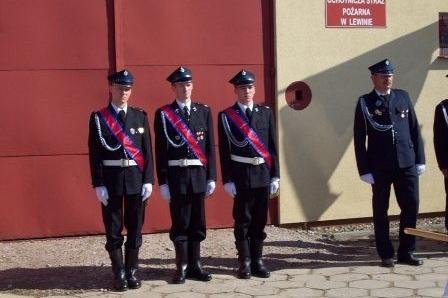 Druhowie OSP Lewino w galowych mundurach z szarfami stoją na zbiórce.
