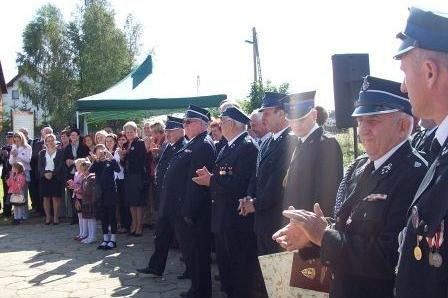 Uroczystość OSP Lewino: strażacy w mundurach i zgromadzeni goście podczas ceremonii na zewnątrz.