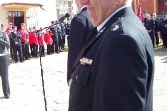 Strażak OSP Lewino w mundurze salutuje podczas uroczystości sztandarowej.
