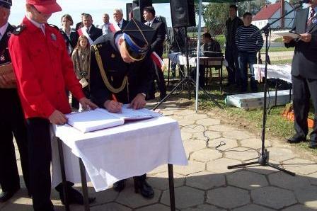 Na ceremonii OSP Lewino osoba w czerwonej czapce obserwuje podpisywanie dokumentu.
