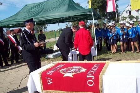 Strażak przy stole z czerwonym sztandarem OSP Lewino podczas uroczystości.