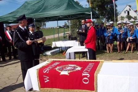 Strażacy OSP Lewino podczas ceremonii; na stole leży czerwony sztandar.
