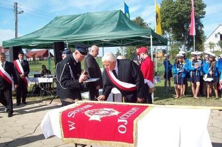 Oficjalna ceremonia przekazania sztandaru OSP Lewino z widocznym sztandarem na stole.