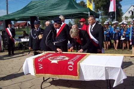 Ceremonia poświęcenia sztandaru OSP Lewino z dostojnikami wokół stołu.