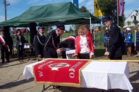 Uroczystość przekazania sztandaru OSP Lewino z ludźmi pochylonymi nad stołem.
