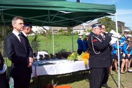 Uroczystość OSP Lewino: strażak w mundurze i mężczyzna w garniturze pod namiotem.