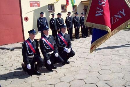 Strażacy OSP Lewino klęczą przed sztandarem, inni stoją w tle.