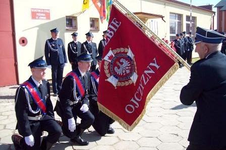 Strażacy OSP w galowych mundurach ze sztandarem na uroczystości.