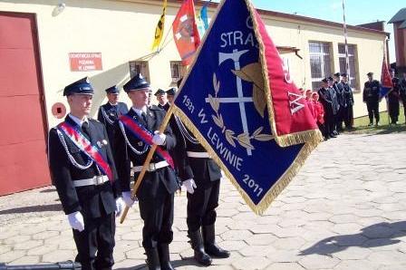 Członkowie OSP Lewino w mundurach prezentują sztandar na zewnątrz.