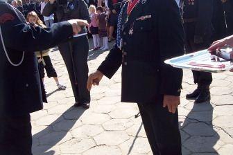 Uścisk dłoni członków OSP Lewino w mundurach, jeden w kapeluszu, na tle sztandaru.