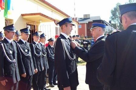 Uroczystość OSP Lewino: strażak przypina medal koledze w mundurze.