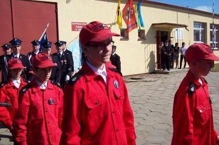 Młodzi strażacy z OSP Lewino w czerwonych mundurach podczas uroczystości.