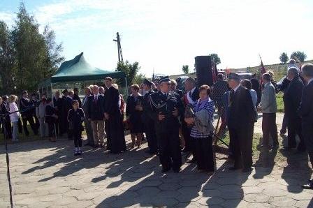 Ludzie na placu podczas uroczystości OSP Lewino w słonecznej pogodzie.