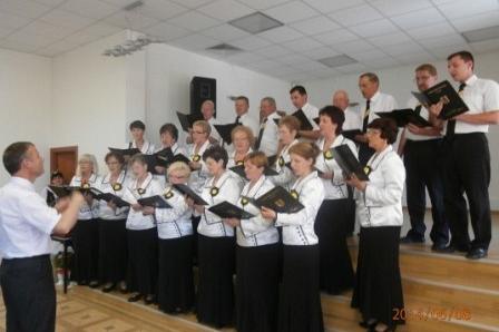 Chór śpiewa z nutami pod batutą dyrygenta w Domu Kultury w Dębogórzu.