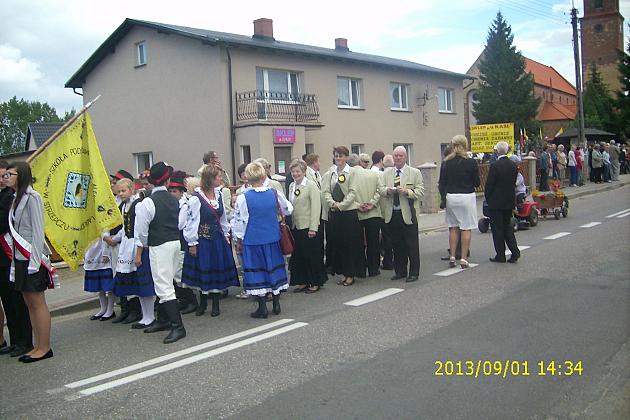 Korowód dożynkowy z ludźmi w tradycyjnych strojach i flagami.