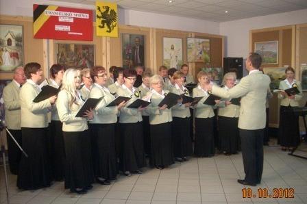 Chór śpiewa z dyrygentem trzymając nuty, na występie w GDK Linia.