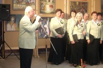 Chór z dyrygentem podczas występu, obok leży instrument strunowy.