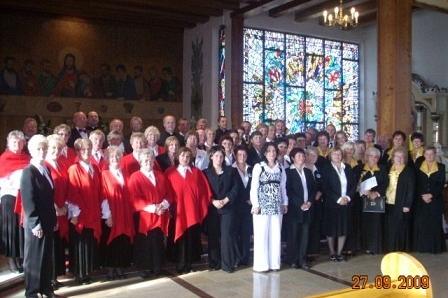 Duża grupa chórzystów w galowych strojach pozuje w kościele podczas przeglądu.