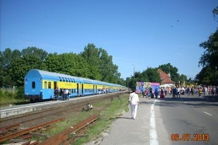 Kaszubski pociąg w barwach regionu na torach, pieszy na drodze w słonecznym Władysławowie.