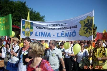 Uczestnicy Zjazdu Kaszubów z transparentem Linia - Łebień pod błękitnym niebem.