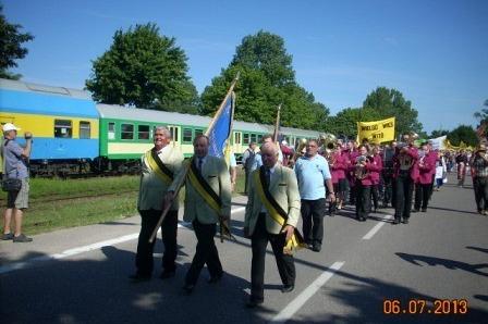 Uczestnicy Zjazdu Kaszubów maszerują z flagą pod niebieskim niebem.