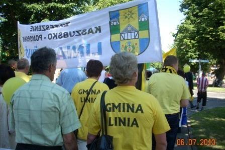 Uczestnicy Zjazdu Kaszubów z Gminy Linia niosący baner z herbem na tle zieleni.