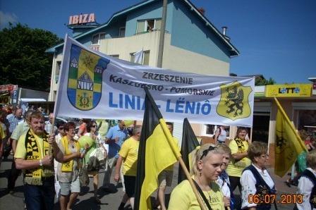 Uczestnicy Zjazdu Kaszubów w żółtych strojach z banerem Gminy Linia i flagami.