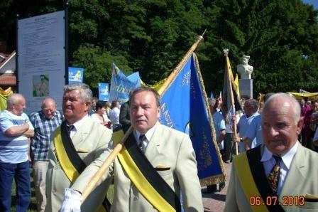 Mężczyźni w tradycyjnych strojach z szarfami maszerują na Zjeździe Kaszubów.