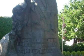 Duża, ciemna rzeźba przypominająca dzwon, z zielonym tłem, widziana z niskiej perspektywy.