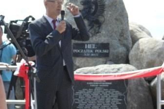 Ceremonia odsłonięcia kaszubskiego kopca z przemawiającym mężczyzną i czerwoną wstęgą.